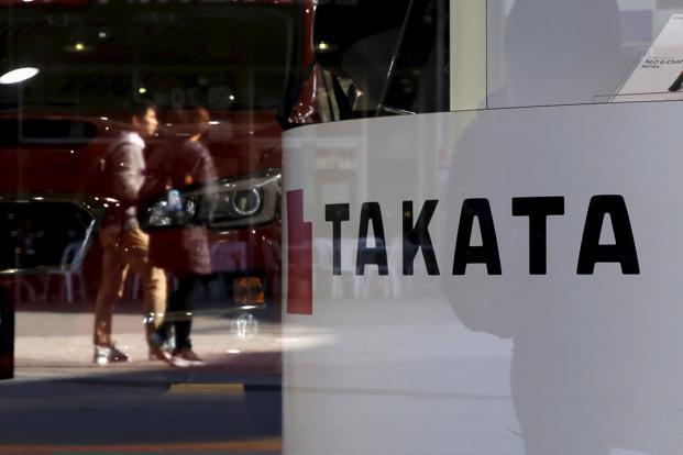 A logo of Takata Corp is seen with its display as people are reflected in a window at a showroom for vehicles in Tokyo