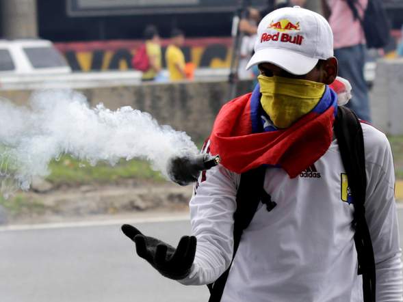 An opposition supporter catches a tear gas bomb during clashes with riot policemen in a rally to demand a referendum to remove President Nicolas Maduro in Caracas