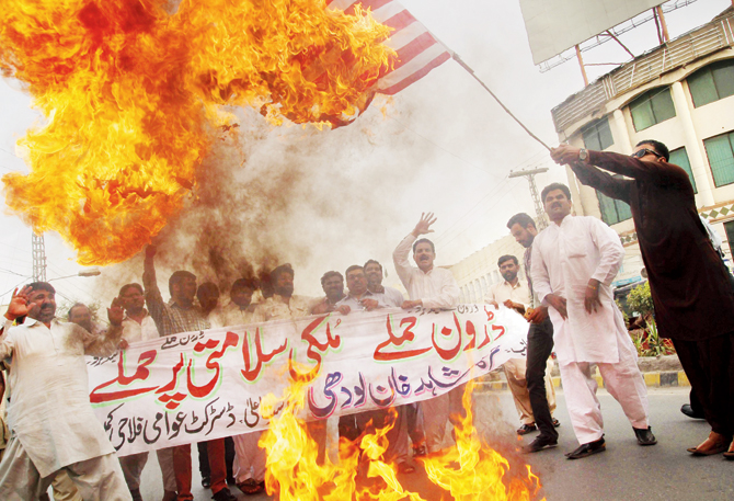 A Pakistani demonstrator holds a burning US flag as others shout slogans during a protest in Multan against the drone strike. Pic  AFP