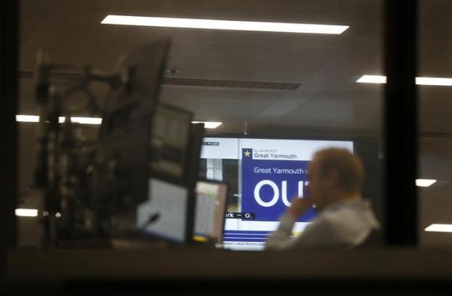 A traders works as EU Referendum results come in on a giant screen behind in London Britain