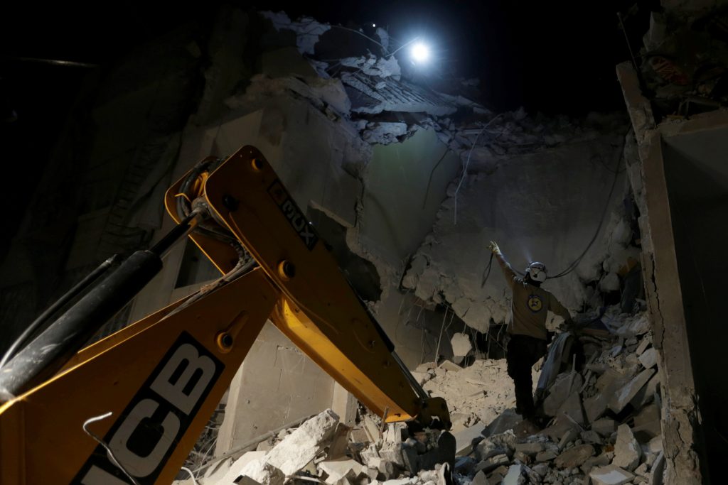 A civil defence member gestures to a fellow member near an excavator as they look for survivors at a site damaged after Russian air strikes on the Syrian rebel-held city of Idlib Syria early