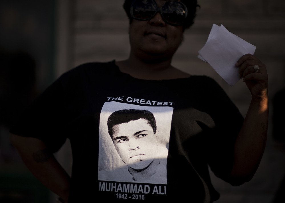 A ray of sunlight shines on a Muhammad Ali shirt worn by Nicole Morris Cowherd as she attends a community memorial service to Ali outside his childhood home Monday in Louisville Ky