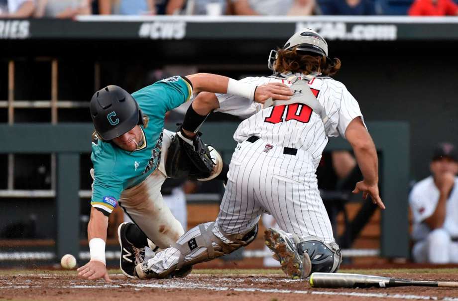 Coastal Carolina's Zach Remillard reaches to score around Texas Tech catcher Tyler Floyd as the ball gets away at home plate in the third inning of an NCAA College World Series baseball game in Omaha Neb. Thursday