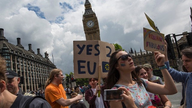 469699542-woman-holds-a-sign-as-other-protesters-gather-outside-1