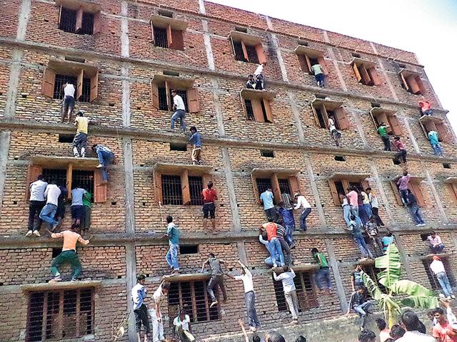 Family members and friends climb walls to make answer chits available to those appearing for their Class 10 exams at a centre in Vaishali Bihar