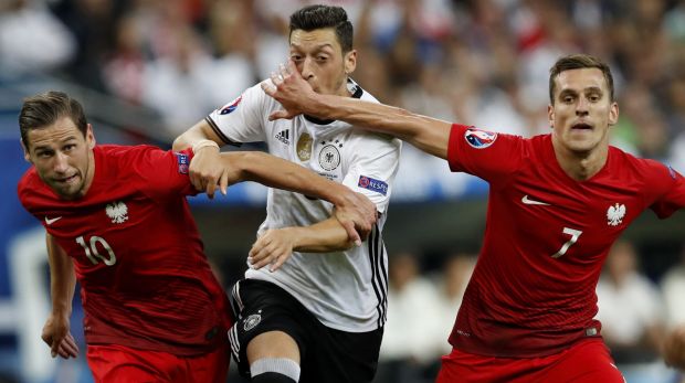 Germany's Mesut Ozil, is challenged by Poland's Grzegorz Krychowiak and Arkadiusz Milik