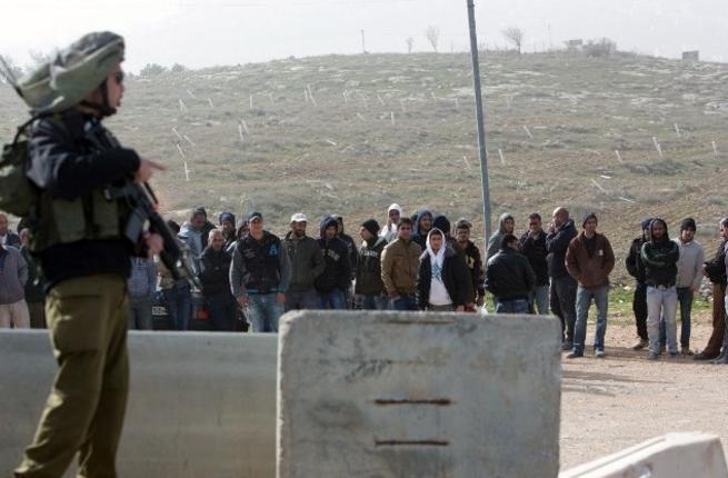 An Israeli soldier stands guard next to Palestinian workers who were transported out of the Tekoa settlement south of Jerusalem following a terror attack in the community