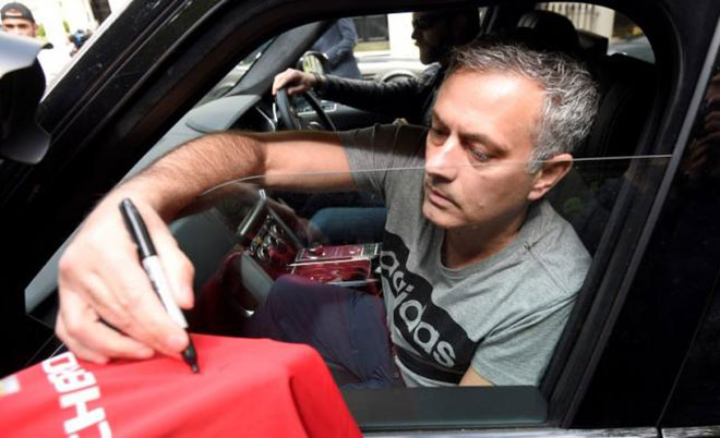 Jose Mourinho signs a Manchester United soccer shirt held out by a fan as he leaves his house in London Britain