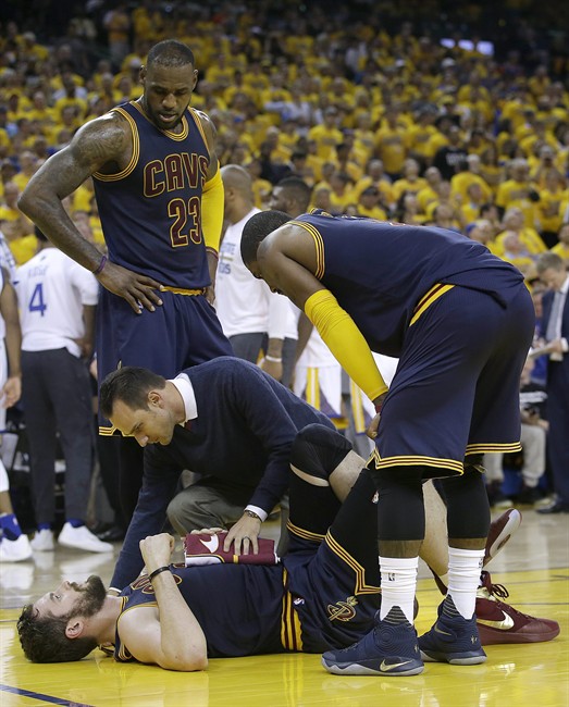 A trainer checks on Cleveland Cavaliers forward Kevin Love bottom as forward Le Bron James and guard Kyrie Irving watch during the first half of a Game 2 of basketball's NBA Finals against the Golden State Warriors in Oakland Calif. Sunday June 5