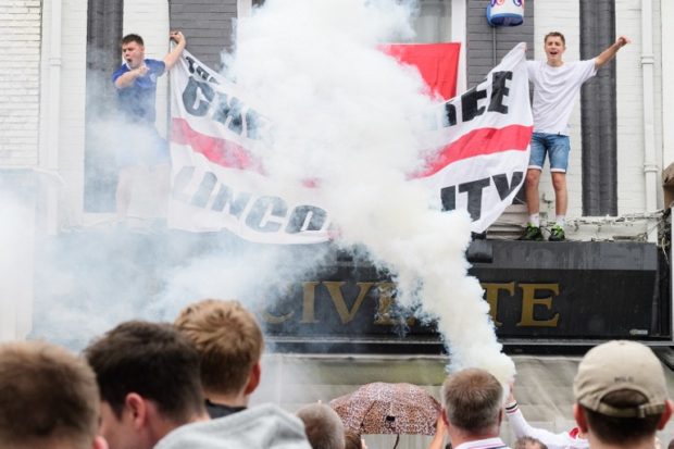 A flare is ignited as England fans hang a flag onto a bar's canopy in central Lens on 16 June 2016 on the day that England plays Wales during the Euro 2016 football tournament.  AFP