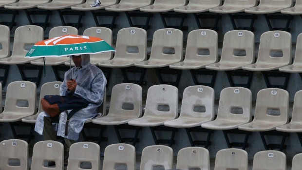 A spectator sits under an umbrella at Suzanne Lenglen court as play again was delayed by rain at Roland Garros