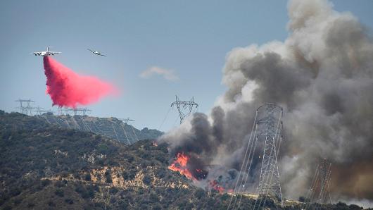 A fire fighting aircraft drops fire retardant as its spotting plane follows above power lines over one of two wildfires in the Angeles National Forest above Azusa California