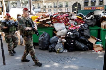 Soldiers pass by a pile of rubbish bags on the Grands boulevards in Paris France during a strike by garbage collectors and sewer workers of the city of Paris to protest the labour reforms law proposal