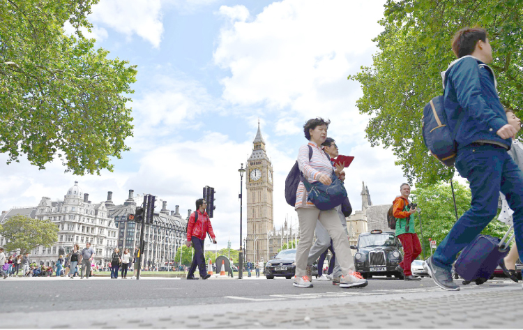 Pedestrians cross a road in front of the Big Ben clock face and the Elizabeth Tower at the Houses of Parliament in central London on Sunday. — AFP