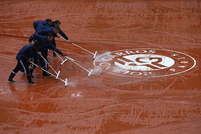 Stadium employees remove water on center court at the French Open tennis tournament at the Roland Garros stadium Tuesday