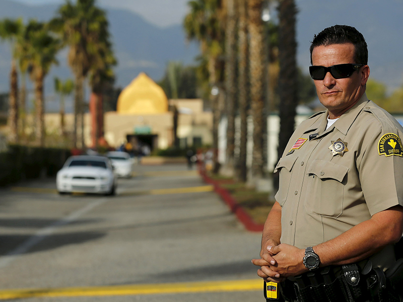 A police officer stands watch as people leave Friday prayers at the Dar Al Uloom Al Islamiyah Amer mosque where shooting suspect Syed Rizwan Farook was seen two to three times a week at lunch time in San Bernardino California