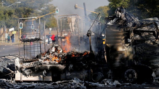 Locals walk past a shell of a burnt out truck used to barricade roads by protesters in Pretoria South Africa