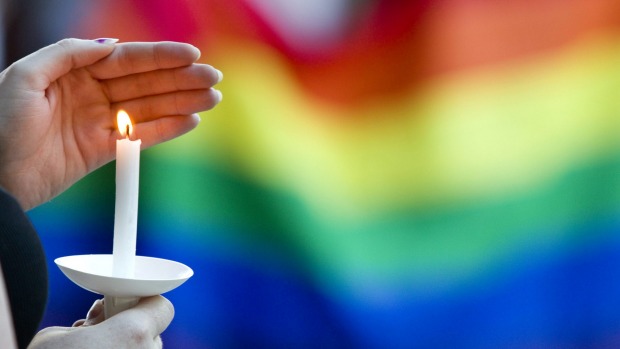 A candle burns in front of a pride flag while community members gather for a vigil to honor the victims of the attack