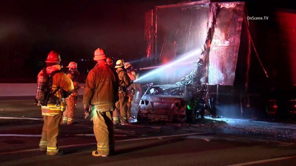 Firefighters work to put out any residual flames after a car and trailer of a big rig burst into flames during a crash on the 101 Freeway in Agoura Hills on Tuesday