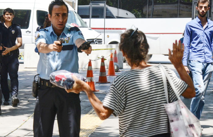 A Turkish police points his gun at a woman asking her to leave the package she is carrying in front of the court house in Ankara on Monday. — AFP