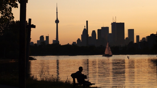 A man sits on a bench in front of the Toronto skyline during sunset at Ashbridge's Bay Park in Toronto