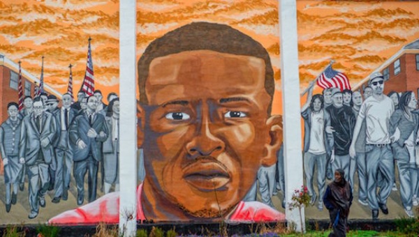 A man who declined to offer his name walks past a mural of Freddie Gray in the Sandtown Winchester neighborhood of Baltimore