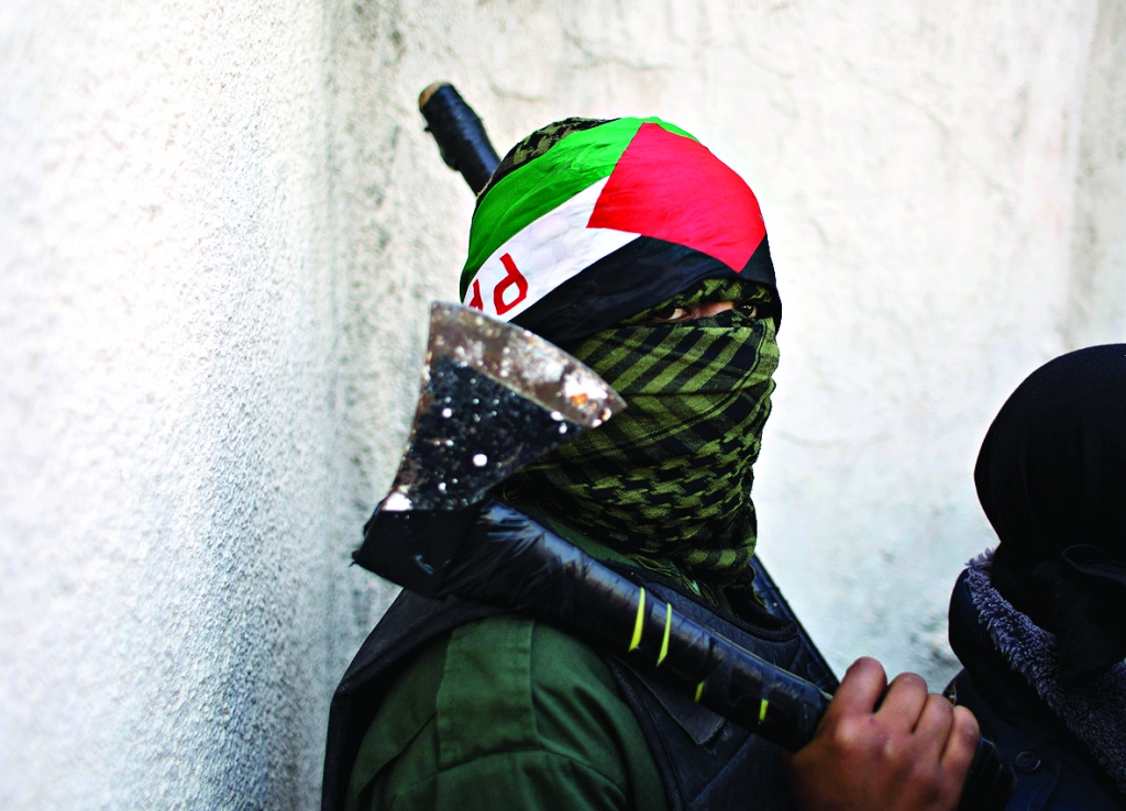 A masked Palestinian youth carries an axe in the Palestinian West Bank refugee camp of Jalazoun Ramallah