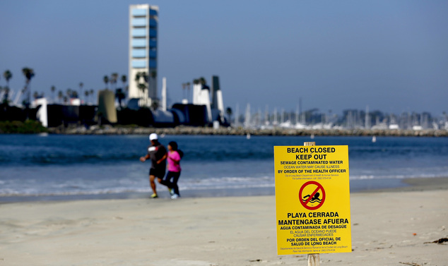 A sign is posted on a beach warning of the dangers of sewage contaminated water Tuesday