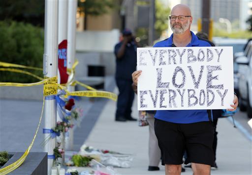 Chris Bailey walks by a makeshift memorial on Griffin Street holding a sign that reads'Everybody Love Everybody, Friday