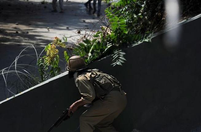 An Indian policeman prepares to fire a pellet gun towards Kashmiri protestors during clashes in Srinagar