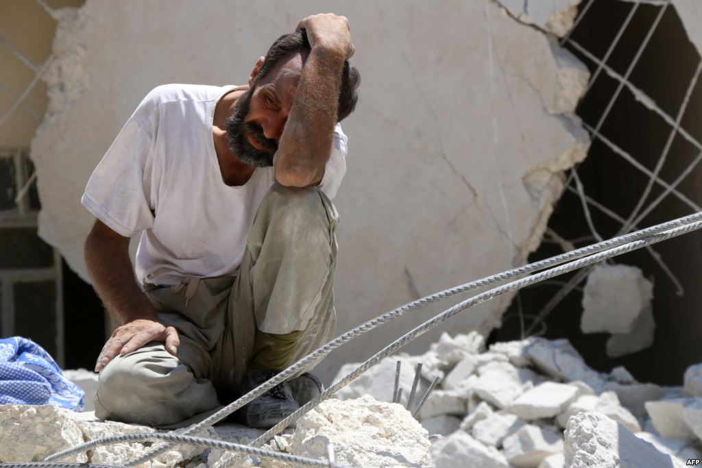 FILE- A man looks on as Syrian civil defense workers look for survivors under the rubble of a collapsed building following reported airstrikes in the rebel-controlled neighborhood of Karm Homad in Aleppo