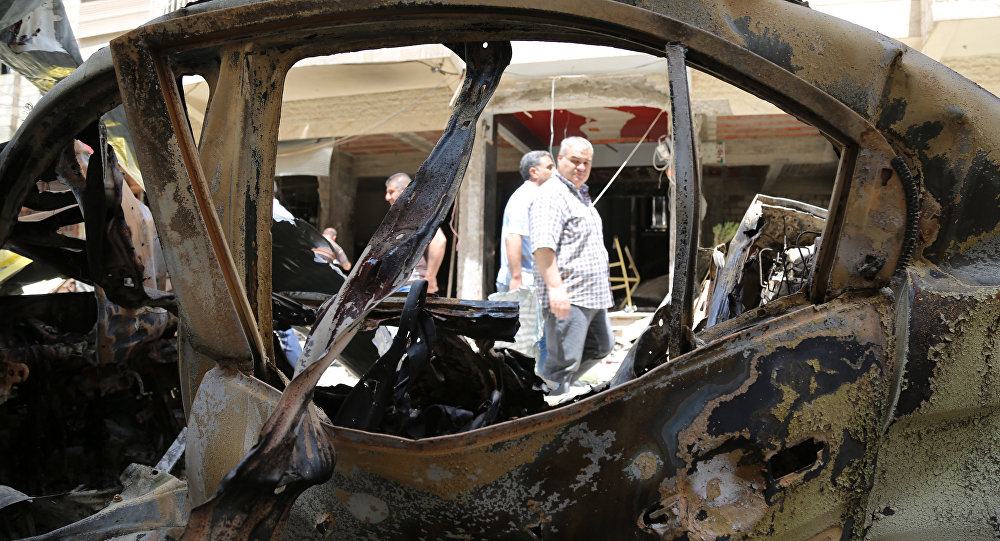 People walk past a burnt vehicle at the site of a suicide bombing suspected to have been carried out by the Islamic State group in the Christian Wusta neighbourhood of the divided Syrian northeastern city of Qamishli