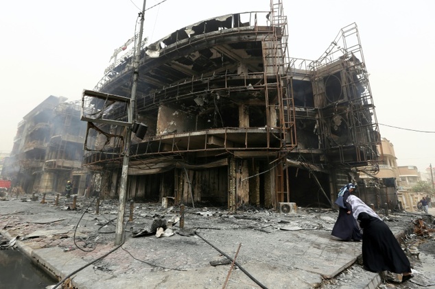 Iraqi women walk past a damaged building at the site of a suicide car bombing claimed by the Islamic State group