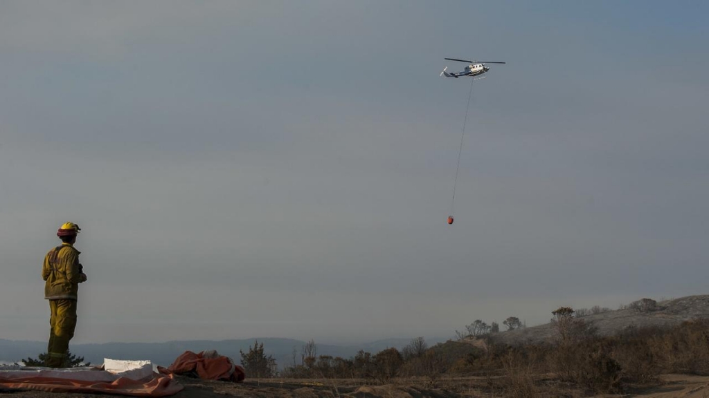 A firefighter watches a helicopter prepare to drop water on a wildfire near Carmel Highlands south of Monterey Calif. Wednesday