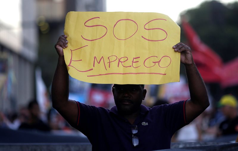 A man holds a banner which reads'S.O.S. employment as he attends a protest on the Rio de Janeiro economic crisis Brazil