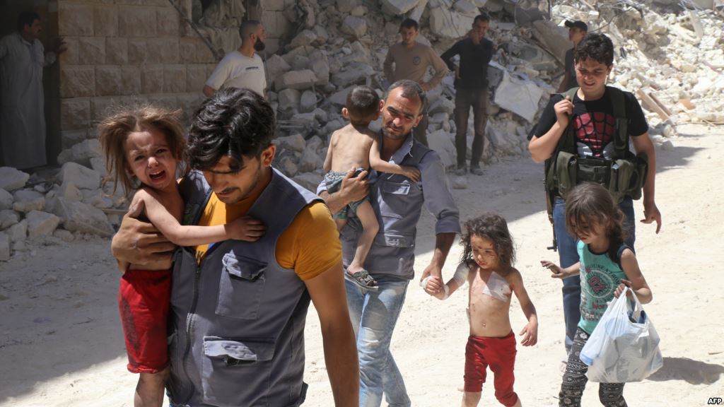 Syrian men carry injured children amid the rubble of destroyed buildings following reported air strikes on the rebel-held neighborhood of Al Mashhad in the northern city of Aleppo on July 25