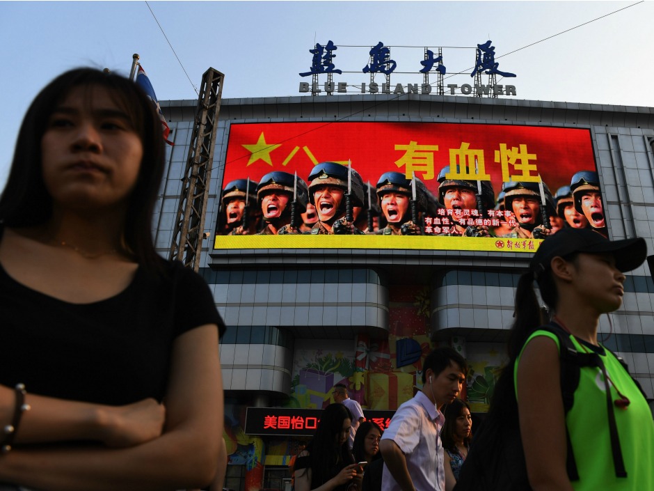 People wait to cross a road in front of an electronic billboard urging a new generation of revolutionary soldiers at a shopping mall in Beijing