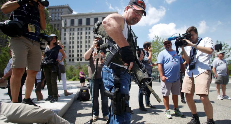 Steve Thacker carrying a rifle and a handgun is surrounded by news media in a public square in Cleveland Ohio U.S