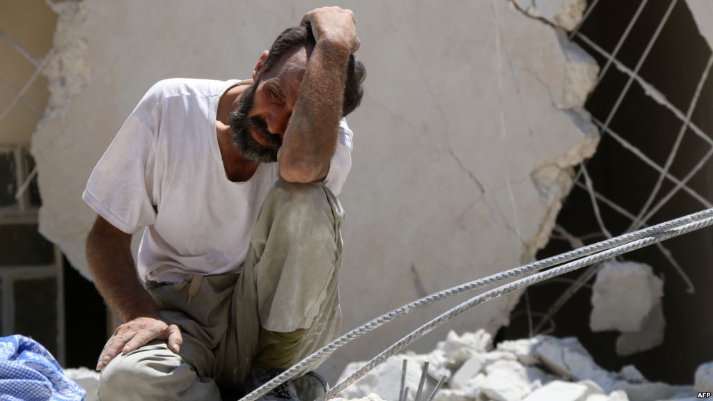 A man looks on as Syrian civil defense workers look for survivors under the rubble of a collapsed building following reported airstrikes