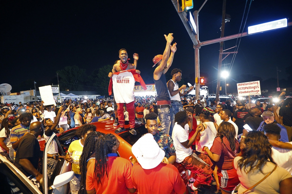 Protesters stand on cars as they congregate at N. Foster Dr. and Fairfields Ave. the location of the Triple S convenience store in Baton Rouge La. Wednesday