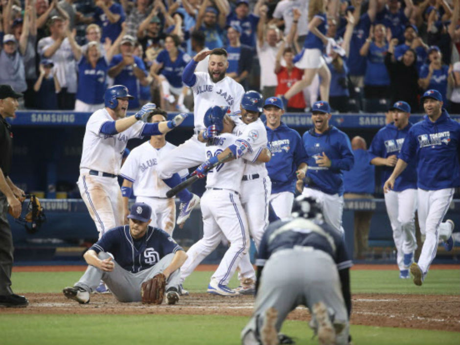 Devon Travis of the Toronto Blue Jays is congratulated by Edwin Encarnacion as Kevin Pillar leaps in the air after their game-winning run scored on a wild pitch in the 12th inning against the San Diego Padres on Tuesday