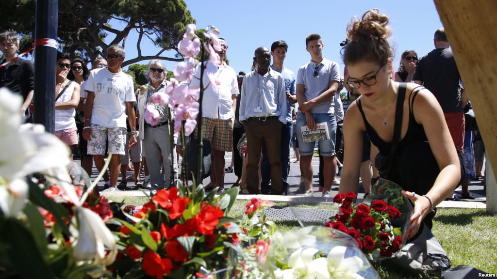 A woman places a bouquet of flowers as people pay tribute near the scene where a truck ran into a crowd at high speed killing scores and injuring more who were celebrating the Bastille Day national holiday in Nice France