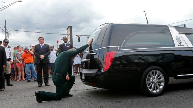 East Baton Rouge Sheriff Sid J. Gautreaux III kneels and places his hand on the casket of deputy Brad Garafola after it was transferred from carriage to hearse at the scene where Garafola and two Baton Rouge police were killed in Baton Rouge La. Sat