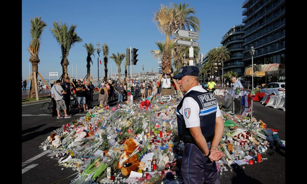 A police officer watches people gathering around a floral tribute for the victims killed during a deadly attack on the famed Boulevard des Anglais in Nice southern France Sunday