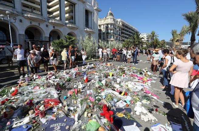 People gather near flowers placed at a makeshift memorial near the Promenade des Anglais in Nice