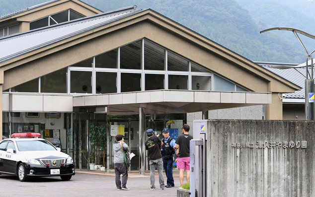 A police officer talks with visitors in front of a facility for the handicapped where a number of people were killed and dozens injured in a knife attack Tue