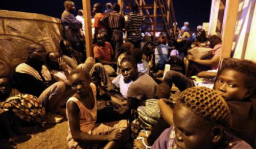 IDP's and villagers huddle for safety from the fighting between buildings on the UN base