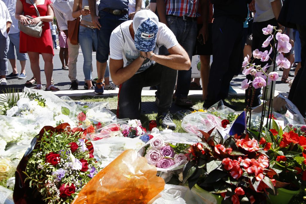 A man reacts near bouquets of flowers as people pay tribute near the scene where a truck ran into a crowd at high speed killing scores and injuring more who were celebrating the Bastille Day national holiday in Nice France