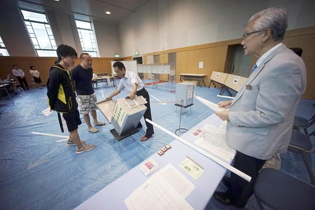 A representative of a local election administration commission shows the earliest two voters the empty ballot box before they cast their votes for Japan's upper house parliamentary elections at a polling station in Tokyo Sunday