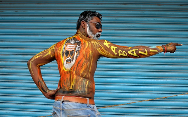 A fan with his body painted with an image of actor Rajinikanth poses outside a movie theatre showcasing the Tamil film